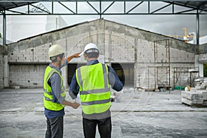 Civil engineers discuss with foreman or builder while holding blueprints and standing under steel structure roof of building at