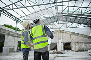 Civil engineers discuss with foreman or builder while holding blueprints and standing under steel structure roof of building at