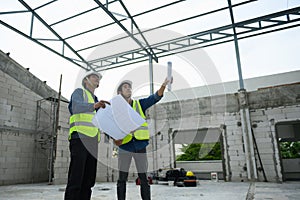 Civil engineers discuss with foreman or builder while holding blueprints and standing under steel structure roof of building at