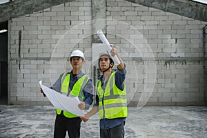 Civil engineers discuss with foreman or builder while holding blueprints and standing under steel structure roof of building at