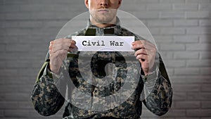 Civil war word written on sign in hands of male soldier, cruelty and death