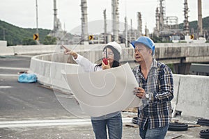Civil woman engineer and construction worker wearing safety hat helmet and holding portable radio with refinery plant background