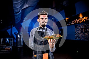 Whiskered waiter offers visitors dish on a black background. photo