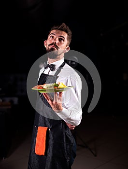 Civilized steward serves plate with prepared dish in the restaurant.