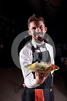 Professional garcon holds salad on a black background. photo