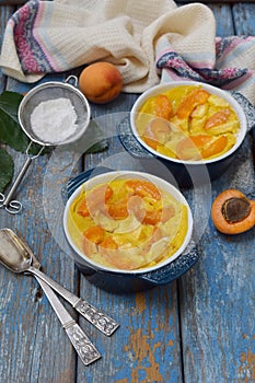 Clafouti with apricots in rameken on blue wooden background. Fruits clafoutis. Sweet casserole. Traditional French cake. Copy