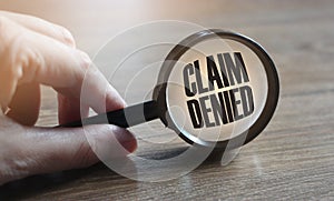 Claim denied in a magnifying glass on a wooden table. Insurance business concept