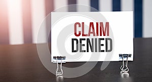 CLAIM DENIED sign on paper on dark desk in sunlight. Blue and white background