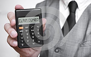 CLAIM DENIED word text inscription on calculator in a male hand of a businessman in white shirt and blue tie, Concept of finance