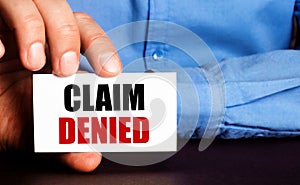 CLAIM DENIED is written on a white business card in a man`s hand. Advertising concept