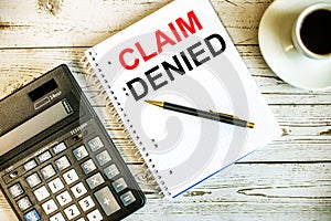 CLAIM DENIED written on white paper near coffee and calculator on a light wooden table. Business concept