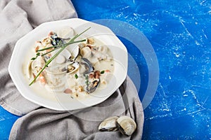Clam chowder in a white plate. The main ingredients are shellfish, broth, butter, potatoes and onions