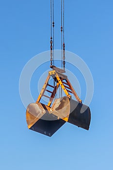 Clamshell bucket suspended by wire ropes and chains against the blue sky