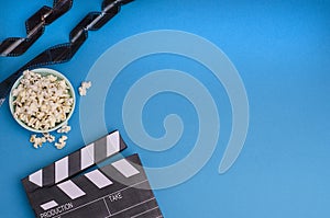 Clapper board with popcorn and film strip on a bright blue background with copy space. For articles about the movie