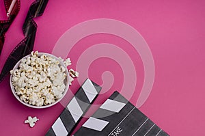 Clapper board with popcorn and film strip on a bright pink background with copy space. For articles about the movie