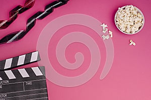 Clapper board with popcorn and film strip on a bright pink background with copy space. For articles about the movie