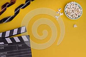 Clapper board with popcorn and film strip on a bright yellow background with copy space. For articles about the movie