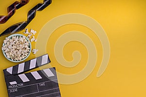 Clapper board with popcorn and film strip on a bright yellow background with copy space. For articles about the movie