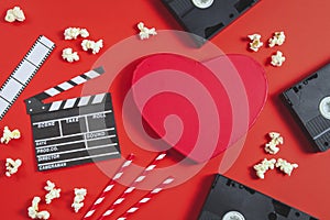 A clapperboard, film strip, popcorn, videotapes, straws and a heart-shaped box lie on a red background.