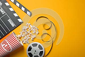 Clapperboard, popcorn and film reel on orange background, flat lay. Space for text