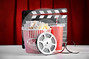 Clapperboard, reel and popcorn bucket on table against stage curtain.