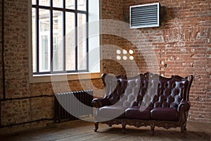 Claret leather sofa to the loft an interior with a bright searchlight and a window. brick wall. ancient pig-iron battery