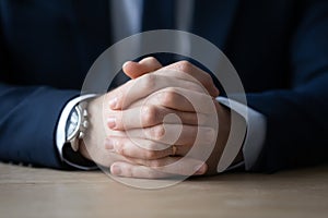 Clasped hands of businessman in formal suit sitting at table