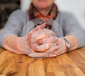 Clasped hands of an elderly lady sitting at a table.