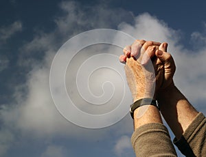 Clasped hands praying. Clouds and sky background.
