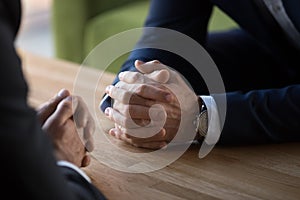 Clasped male hands of two businessmen negotiating at table