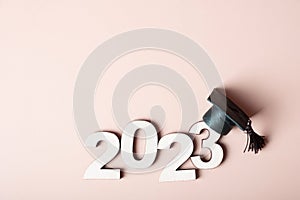 Class of 2023 concept. Wooden number 2023 with graduated cap on colored background