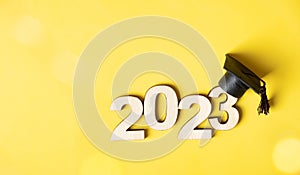 Class of 2023 concept. Wooden number 2023 with graduated cap on colored background with bokeh