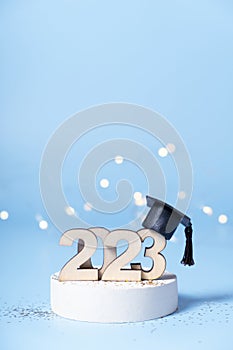 Class of 2023 concept. Wooden number 2023 with graduated cap on podium on colored background