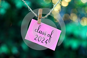 class of 2024 on pink note paper hanging on rope with bokeh background.