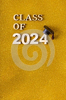 Class of 2024 text with graduated cap on golden glitter background. Graduation holiday concept.