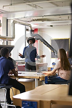 Class Of High School Students Sitting At Work Benches Listening To Teacher In Design And Technology Lesson