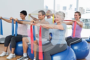 Class holding out exercise belts while sitting on fitness balls