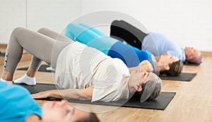 Class of male and women of different ages in active wear doing buttock bridge exercise during Pilates training together