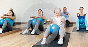 Class of people of different ages holding balls between legs and pushing press during Pilates training in studio
