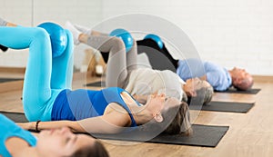 Class of people of different ages holding balls between legs and pushing press during Pilates training in studio