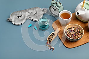 Classic alarm clock, sleeping mask, tea pot on blue pastel background. Minimal concept of rest, quality of sleep, good