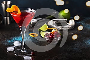 Classic alcoholic cocktail cosmopolitan with vodka, liqueur, cranberry juice, lime, ice and orange zest, dark bar counter