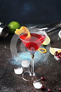 Classic alcoholic cocktail cosmopolitan with vodka, liqueur, cranberry juice, lime, ice and orange zest, dark bar counter