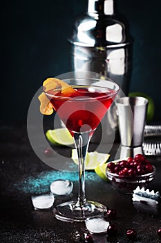 Classic alcoholic cocktail cosmopolitan with vodka, liqueur, cranberry juice, lime, ice and orange zest, dark bar counter