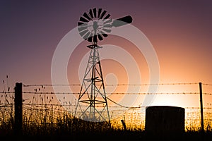 Classic Australian windmill on farmland silhouetted at sunset