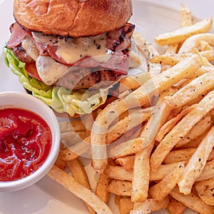 A classic bacon cheeseburger and french fries with ketchup sauce close up.