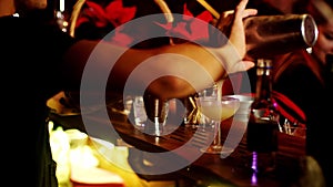 A classic bartender pours sparkling wine from a tall glass into a cocktail glass in the interior of a stylish bar.