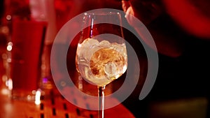 A classic bartender pours sparkling wine from a tall glass into a cocktail glass in the interior of a stylish bar.