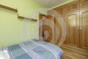 Classic bedroom with a bed covered with a striped bedspread, a large built-in wardrobe with oak wood doors and light green painted