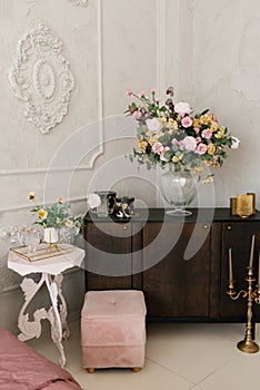 Classic bedroom interior. A brown wooden chest of drawers, flowers in a glass vase, and a white bedside table